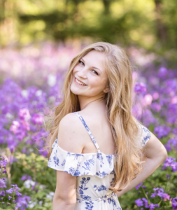A woman smiling with purple flowers surrounding her. 